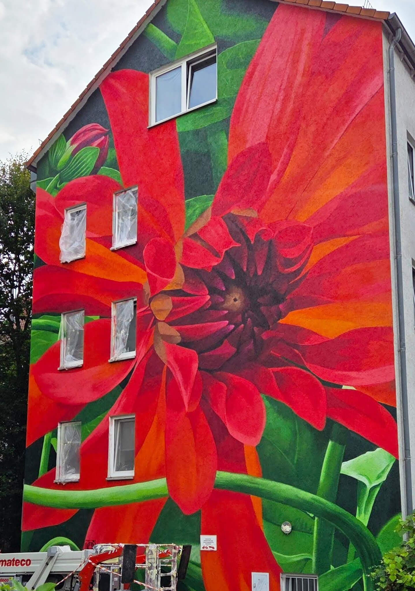 Großflächiges Wandbild einer roten Dahlie mit grünen Blättern an der Fassade eines mehrstöckigen Hauses